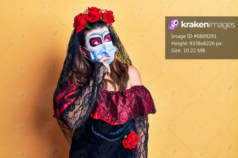 Young woman wearing day of the dead costume wearing medical mask looking stressed and nervous with hands on mouth biting nails. anxiety problem. 