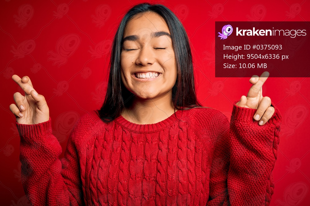 Young beautiful asian woman wearing casual sweater standing over isolated red background gesturing finger crossed smiling with hope and eyes closed. Luck and superstitious concept.
