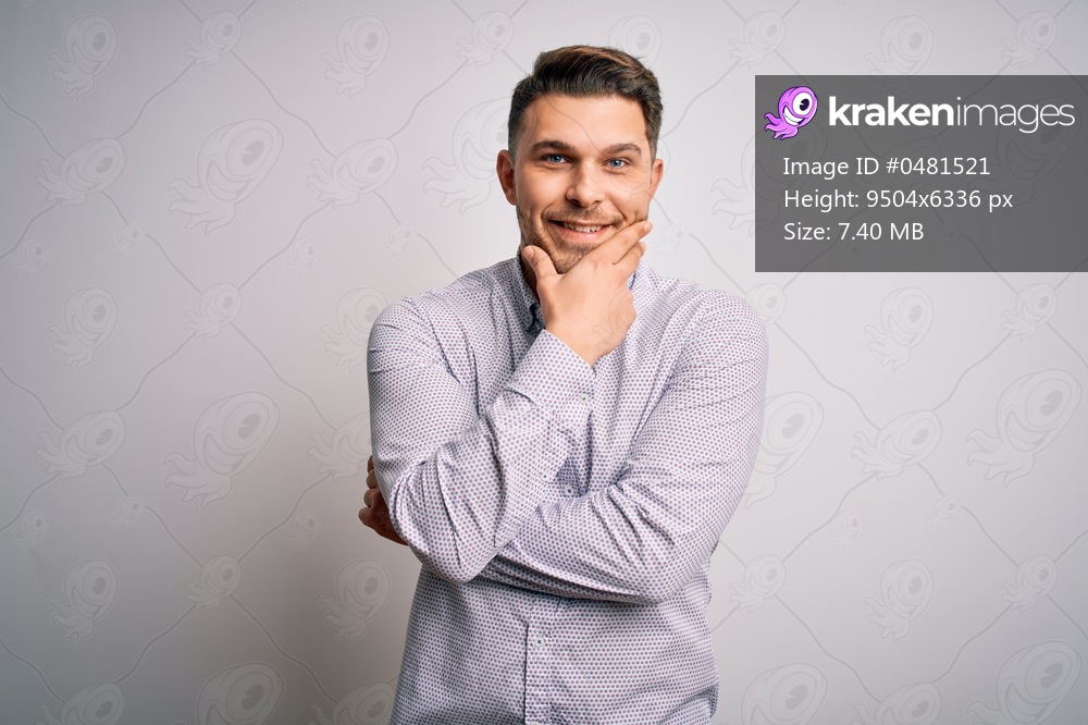 Young business man with blue eyes standing over isolated background looking confident at the camera smiling with crossed arms and hand raised on chin. Thinking positive.