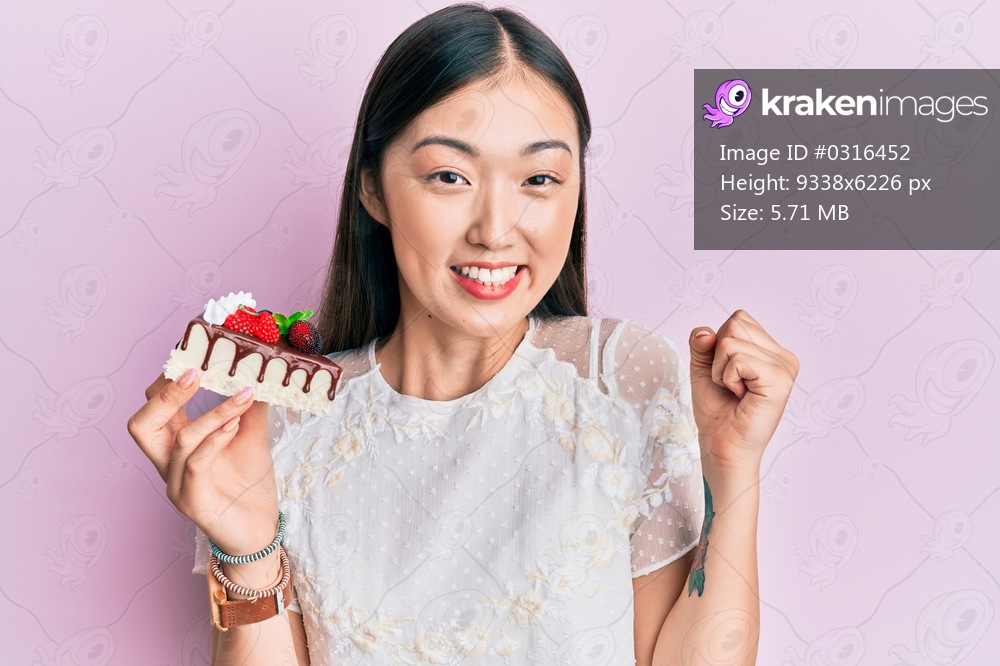 Young chinese woman eating a tasty cake screaming proud, celebrating victory and success very excited with raised arm 