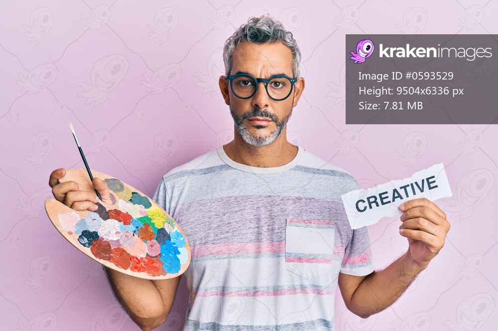 Middle age grey-haired man holding palette and creative message paper relaxed with serious expression on face. simple and natural looking at the camera. 