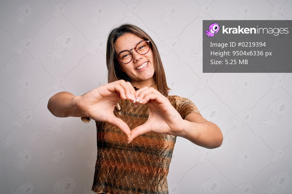 Young beautiful brunette girl wearing casual t-shirt and glasses over isolated white background smiling in love showing heart symbol and shape with hands. Romantic concept.
