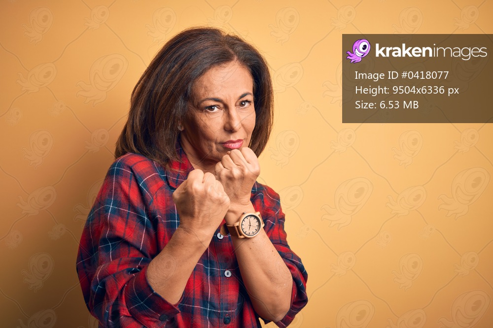 Middle age beautiful woman wearing casual shirt standing over isolated yellow background Ready to fight with fist defense gesture, angry and upset face, afraid of problem