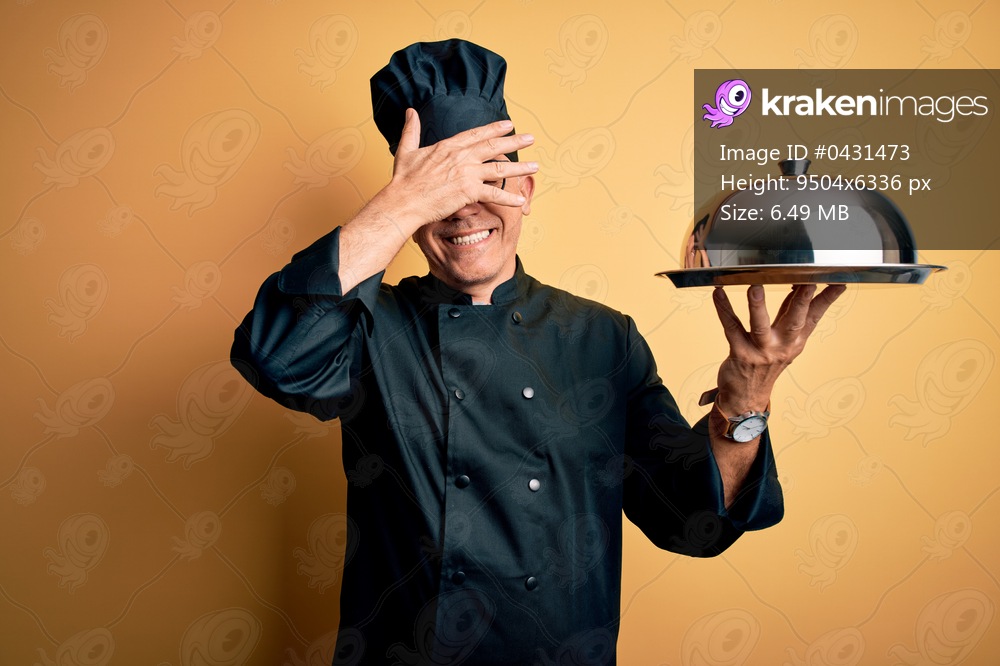 Middle age handsome grey-haired waiter man wearing cooker uniform and hat holding tray smiling and laughing with hand on face covering eyes for surprise. Blind concept.