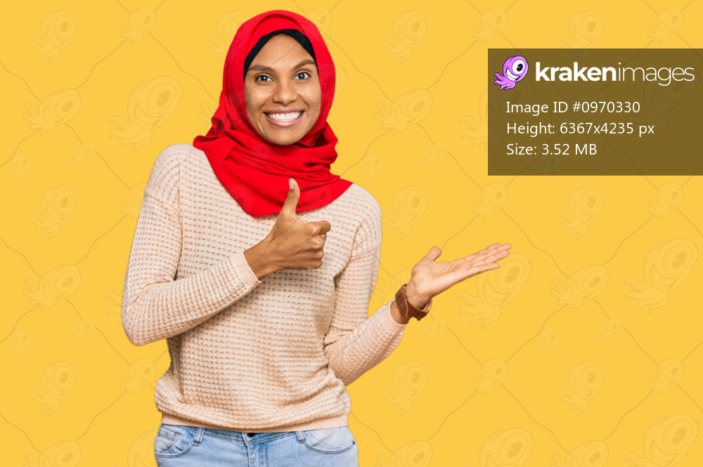 Young african american woman wearing traditional islamic hijab scarf showing palm hand and doing ok gesture with thumbs up, smiling happy and cheerful 