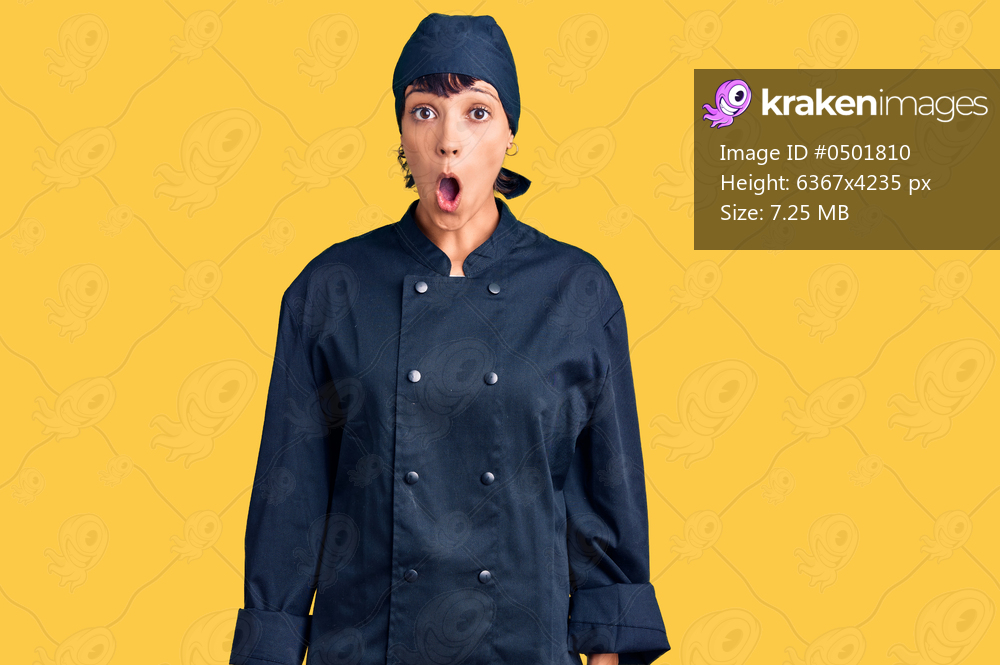 Young brunette woman with short hair wearing professional cook uniform afraid and shocked with surprise expression, fear and excited face. 