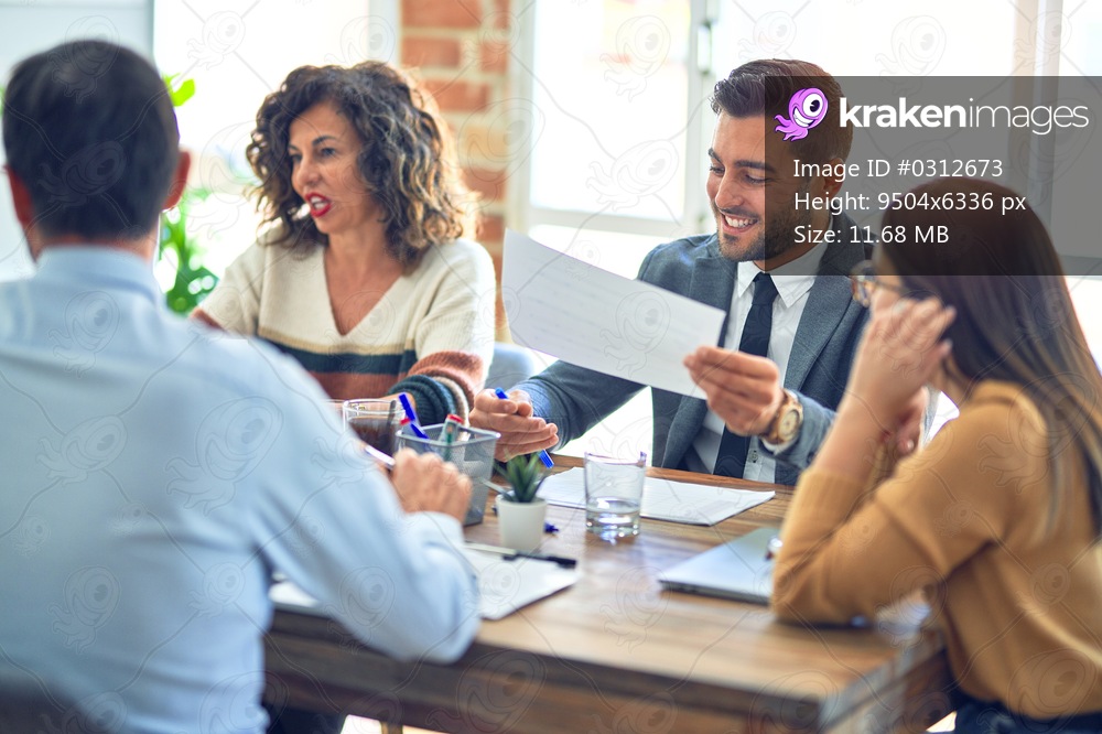 Group of business workers smiling happy working together. Sitting on desk with smile on face reading documents at the office