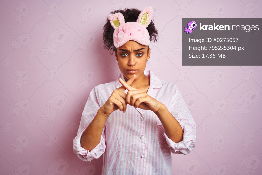 Young african american woman wearing pajama and mask over isolated pink background Rejection expression crossing fingers doing negative sign
