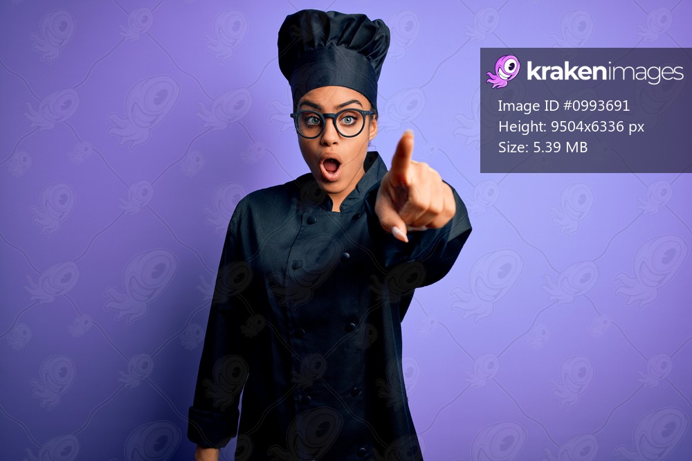 Young african american chef girl wearing cooker uniform and hat over purple background Pointing with finger surprised ahead, open mouth amazed expression, something on the front