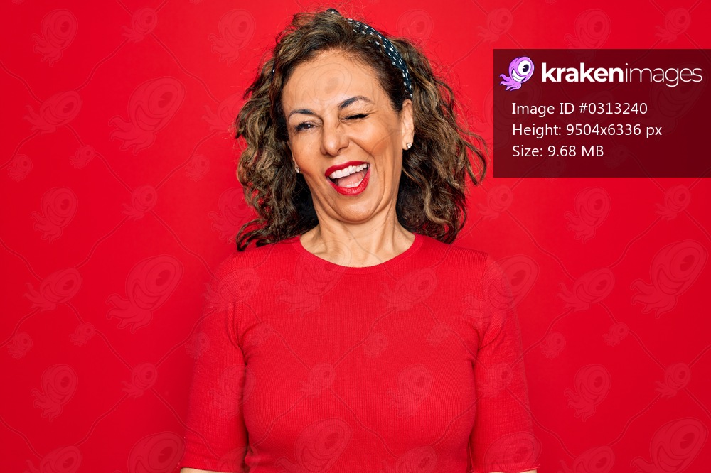 Middle age senior brunette woman wearing casual t-shirt standing over red background winking looking at the camera with sexy expression, cheerful and happy face.
