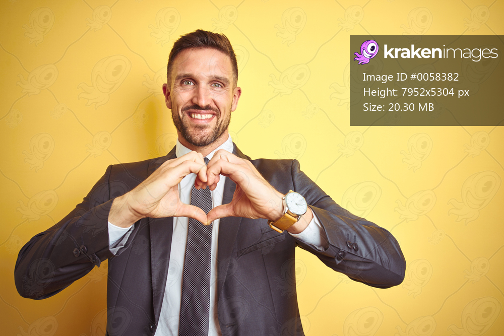 Young handsome business man over yellow isolated background smiling in love doing heart symbol shape with hands. Romantic concept.
