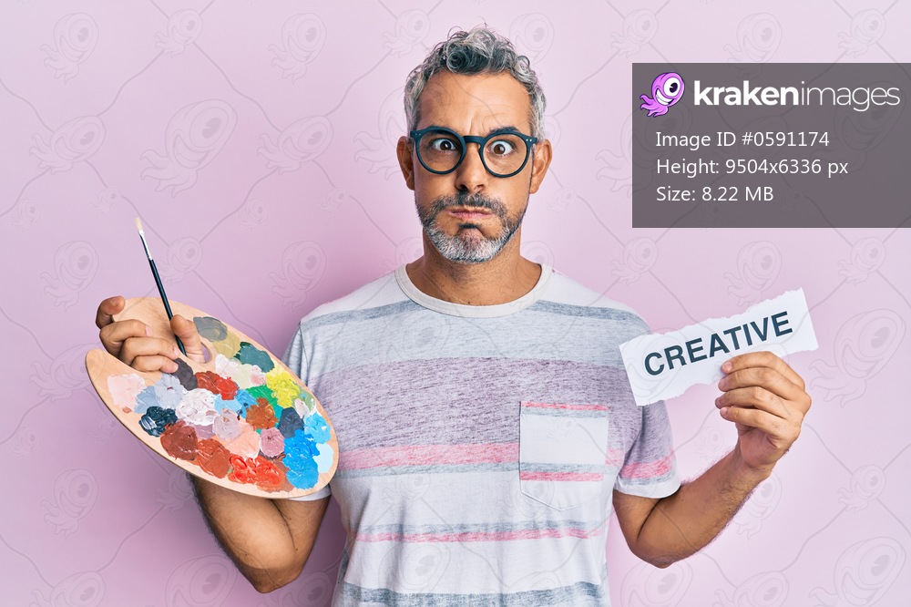 Middle age grey-haired man holding palette and creative message paper puffing cheeks with funny face. mouth inflated with air, catching air. 