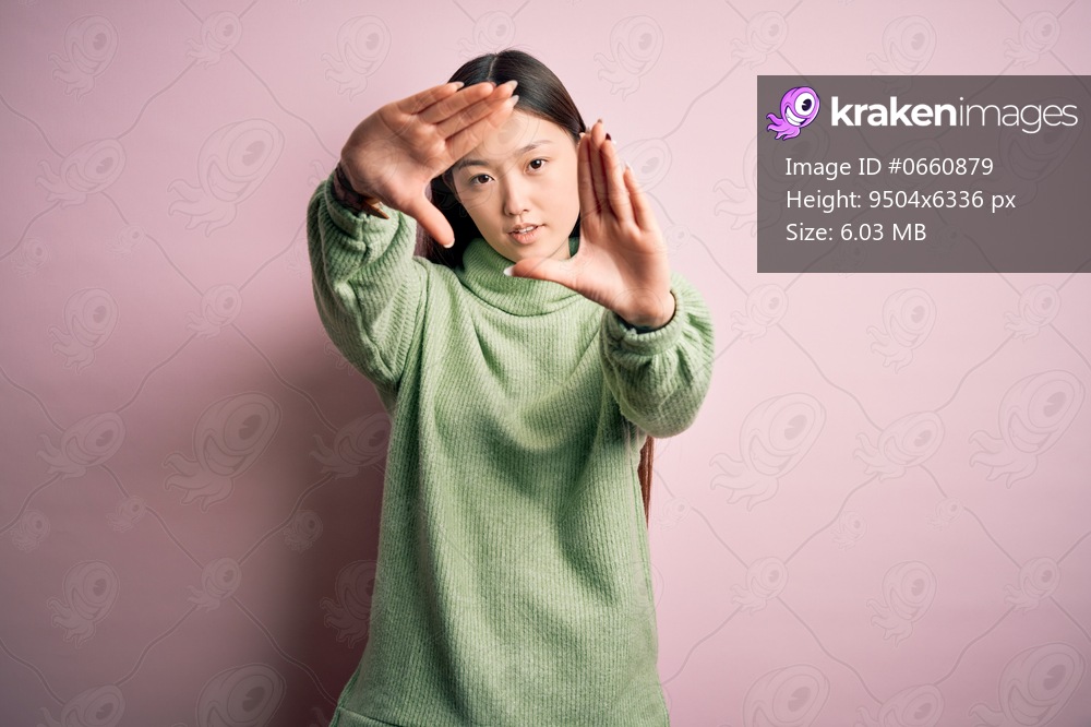 Young beautiful asian woman wearing green winter sweater over pink solated background doing frame using hands palms and fingers, camera perspective