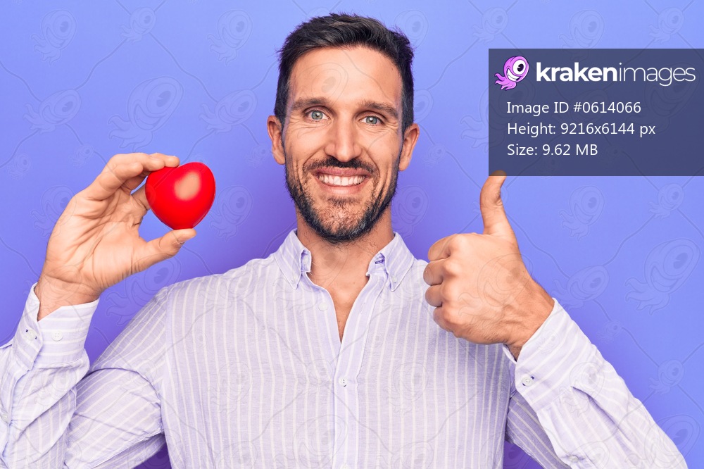 Young handsome man asking for health care holding red heart over isolated purple background smiling happy and positive, thumb up doing excellent and approval sign