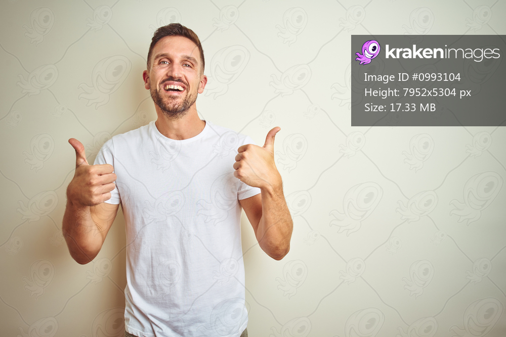 Young handsome man wearing casual white t-shirt over isolated background success sign doing positive gesture with hand, thumbs up smiling and happy. Cheerful expression and winner gesture.