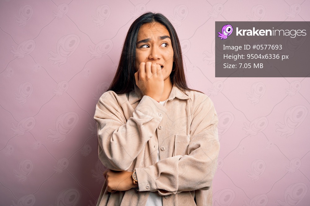 Young beautiful asian woman wearing casual shirt standing over pink background looking stressed and nervous with hands on mouth biting nails. Anxiety problem.