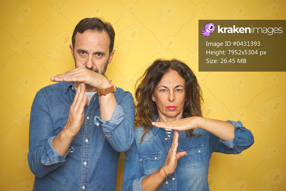 Beautiful middle age couple together standing over isolated yellow background Doing time out gesture with hands, frustrated and serious face