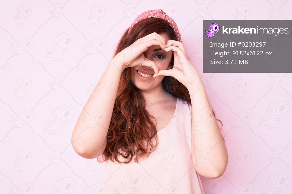 Young beautiful woman wearing casual clothes doing heart shape with hand and fingers smiling looking through sign 