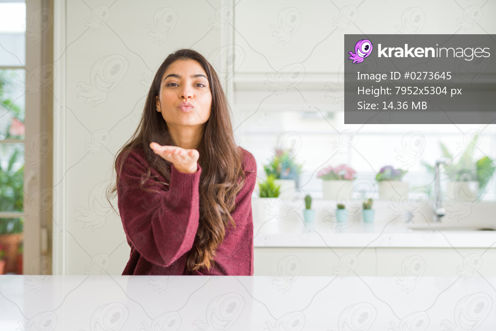 Young beautiful woman at home looking at the camera blowing a kiss with hand on air being lovely and sexy. Love expression.