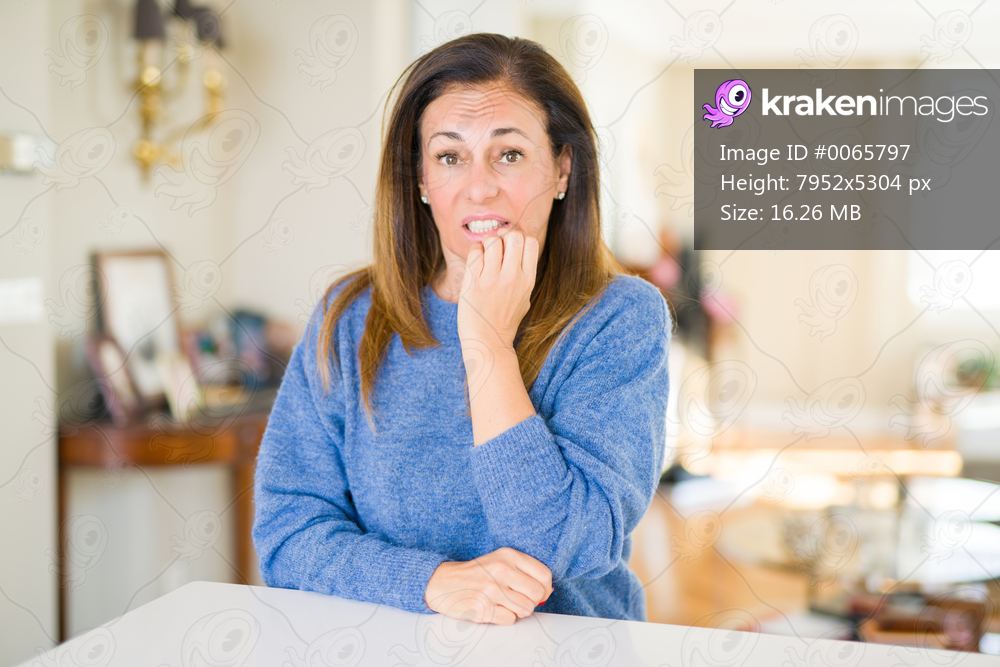 Beautiful middle age woman at home looking stressed and nervous with hands on mouth biting nails. Anxiety problem.