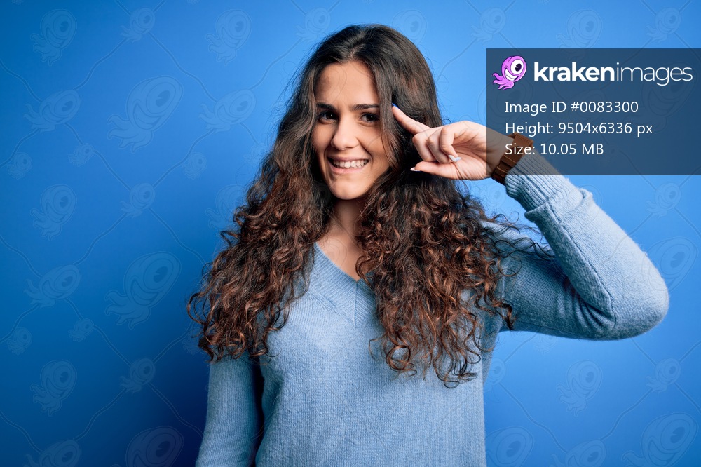 Young beautiful woman with curly hair wearing blue casual sweater over isolated background Smiling pointing to head with one finger, great idea or thought, good memory