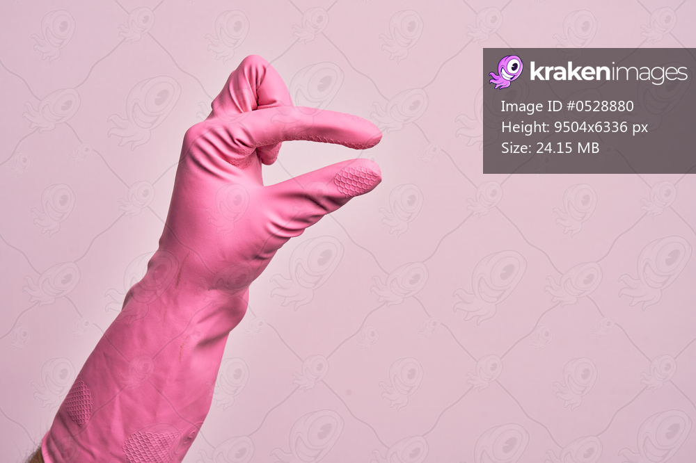 Hand of caucasian young man with cleaning glove over isolated pink background picking and taking invisible thing, holding object with fingers showing space