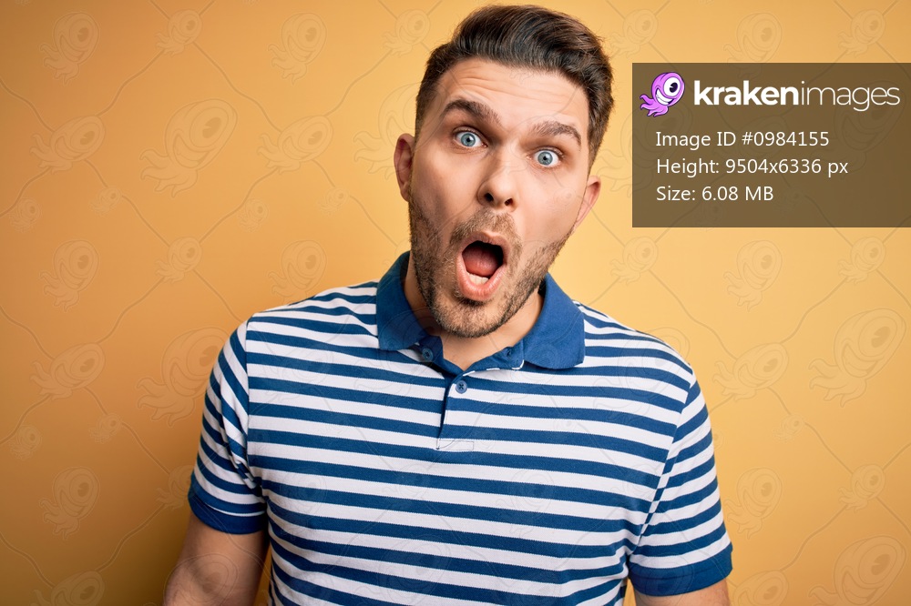 Young man with blue eyes wearing casual striped t-shirt over yellow background afraid and shocked with surprise expression, fear and excited face.