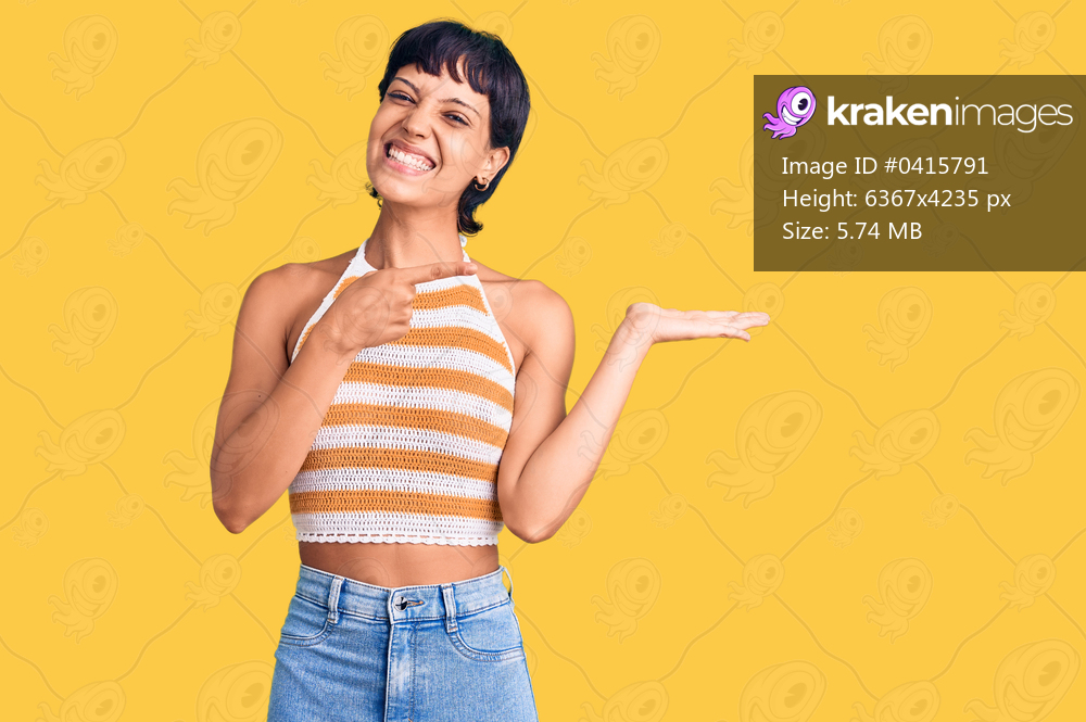 Young brunette woman with short hair wearing casual clothes amazed and smiling to the camera while presenting with hand and pointing with finger. 