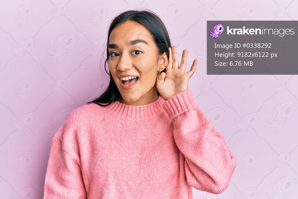 Young asian woman wearing casual winter sweater smiling with hand over ear listening and hearing to rumor or gossip. deafness concept. 