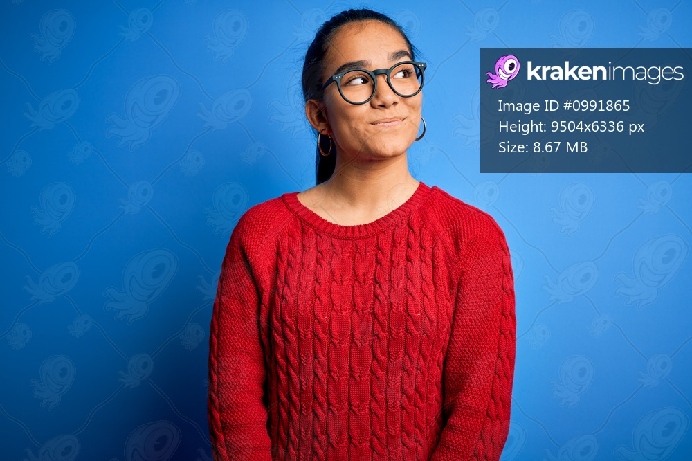 Young beautiful asian woman wearing casual sweater and glasses over blue background smiling looking to the side and staring away thinking.