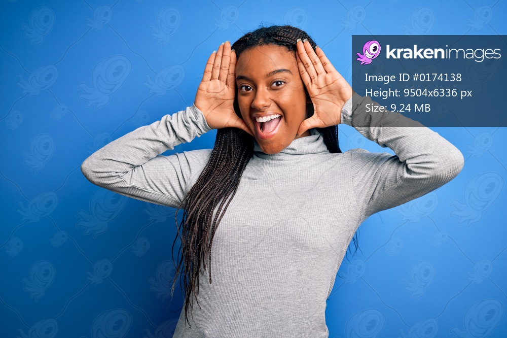 Young african american woman standing wearing casual turtleneck over blue isolated background Smiling cheerful playing peek a boo with hands showing face. Surprised and exited