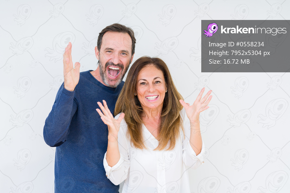 Beautiful middle age couple in love over isolated background celebrating crazy and amazed for success with arms raised and open eyes screaming excited. Winner concept