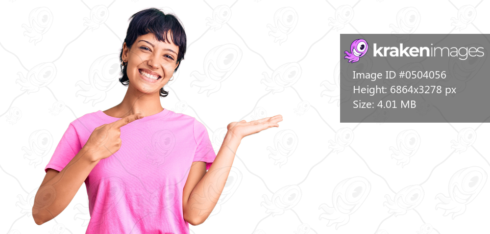 Young brunette woman with short hair wearing casual clothes amazed and smiling to the camera while presenting with hand and pointing with finger. 