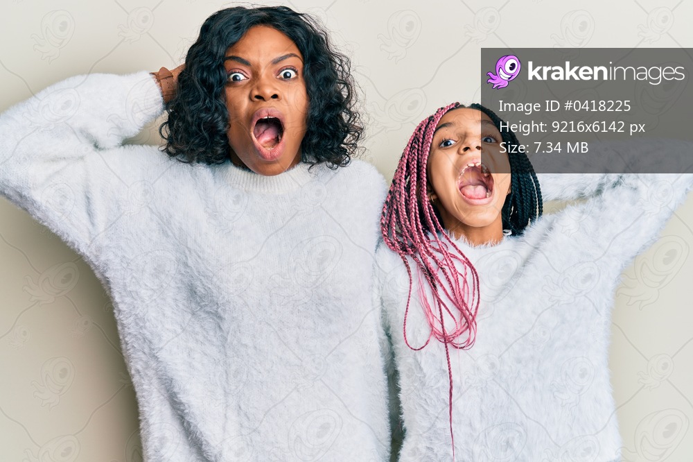 Beautiful african american mother and daughter wearing casual winter sweater crazy and scared with hands on head, afraid and surprised of shock with open mouth 