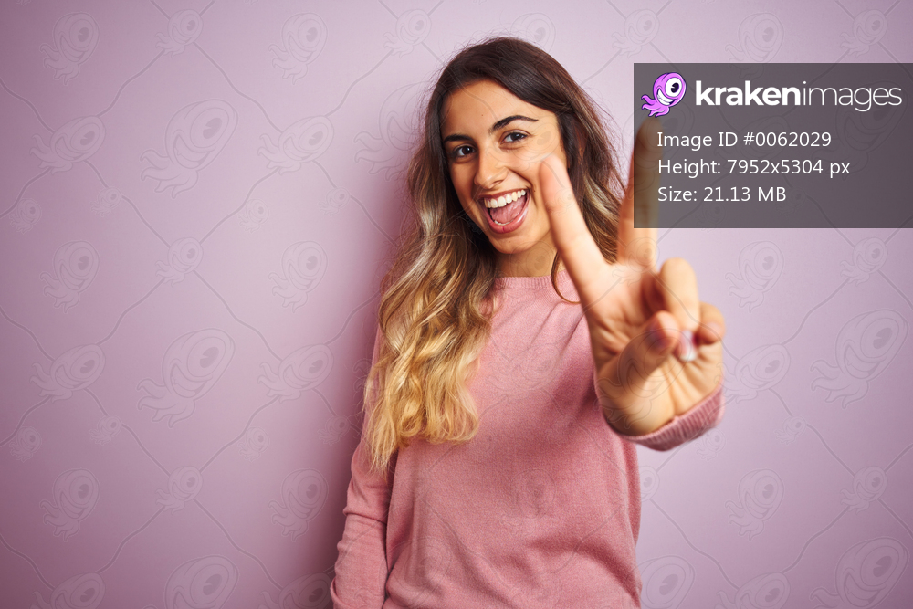 Young beautiful woman wearing a sweater over pink isolated background smiling looking to the camera showing fingers doing victory sign. Number two.
