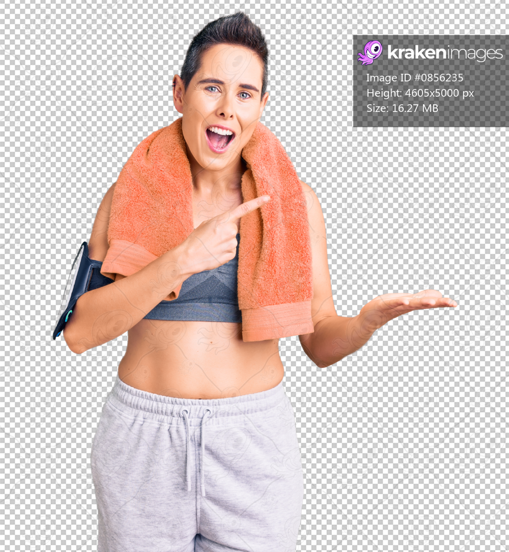 Young woman with short hair wearing sportswear and towel using smartphone amazed and smiling to the camera while presenting with hand and pointing with finger.