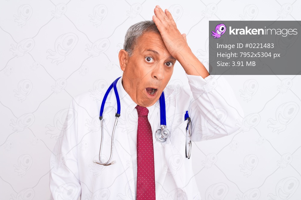 Senior grey-haired doctor man wearing stethoscope standing over isolated white background surprised with hand on head for mistake, remember error. Forgot, bad memory concept.