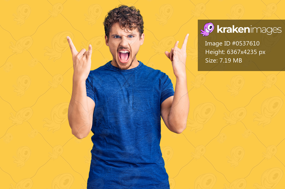 Young handsome man with curly hair wearing casual clothes shouting with crazy expression doing rock symbol with hands up. music star. heavy concept. 