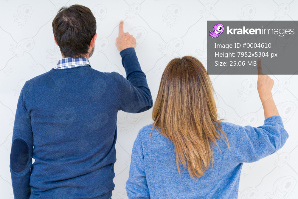 Beautiful middle age couple in love over isolated background Posing backwards pointing behind with finger hand