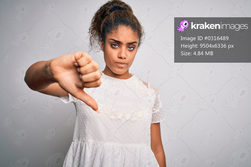 Young beautiful african american girl wearing casual t-shirt standing over white background looking unhappy and angry showing rejection and negative with thumbs down gesture. Bad expression.