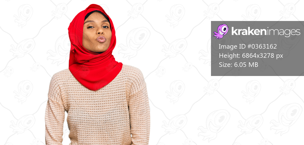 Young african american woman wearing traditional islamic hijab scarf looking at the camera blowing a kiss on air being lovely and sexy. love expression. 