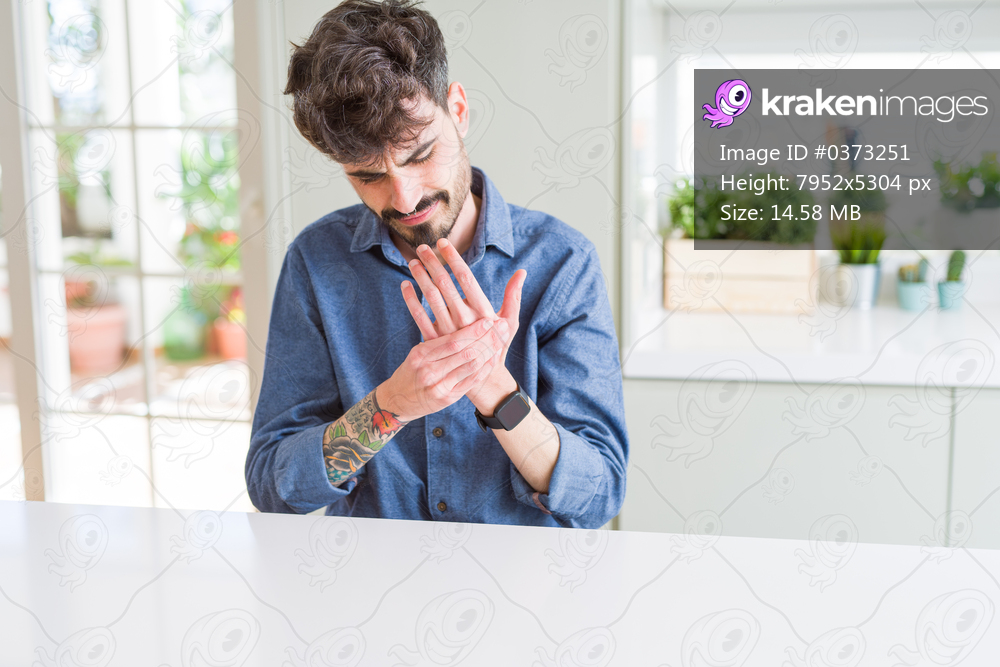 Young man wearing casual shirt sitting on white table Suffering pain on hands and fingers, arthritis inflammation