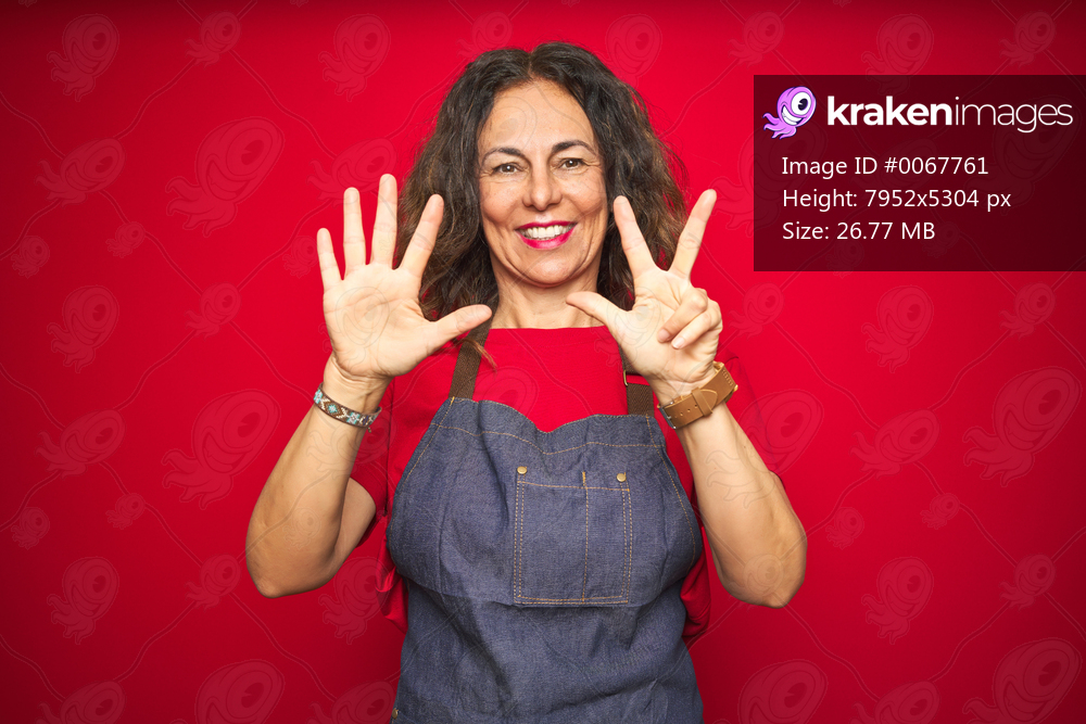 Middle age senior woman wearing apron uniform over red isolated background showing and pointing up with fingers number eight while smiling confident and happy.