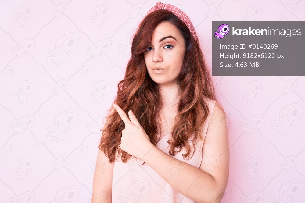 Young beautiful woman wearing casual clothes pointing with hand finger to the side showing advertisement, serious and calm face 