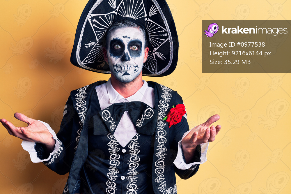 Young man wearing mexican day of the dead costume over yellow clueless and confused expression with arms and hands raised. doubt concept. 