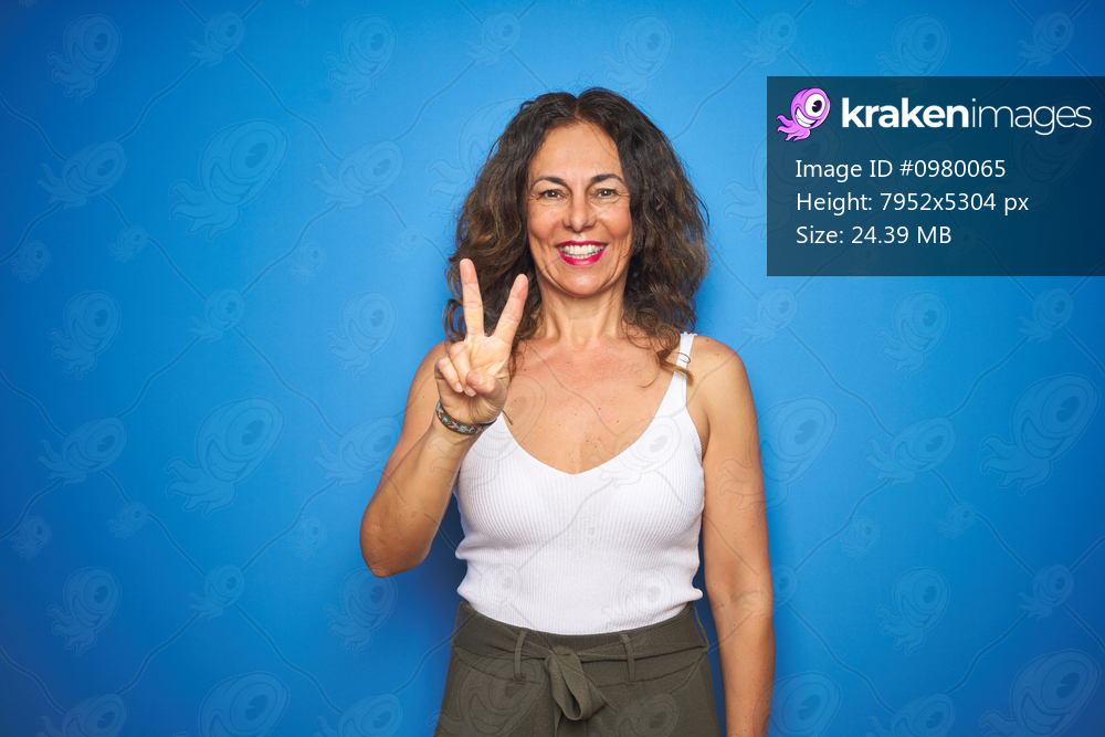 Middle age senior woman with curly hair standing over blue isolated background showing and pointing up with fingers number two while smiling confident and happy.