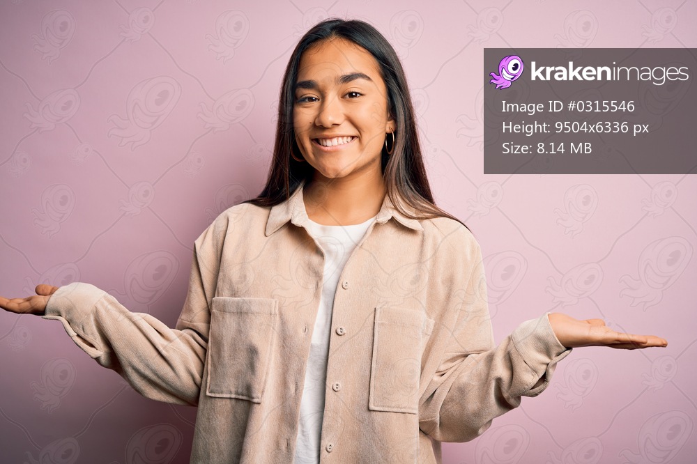 Young beautiful asian woman wearing casual shirt standing over pink background smiling showing both hands open palms, presenting and advertising comparison and balance