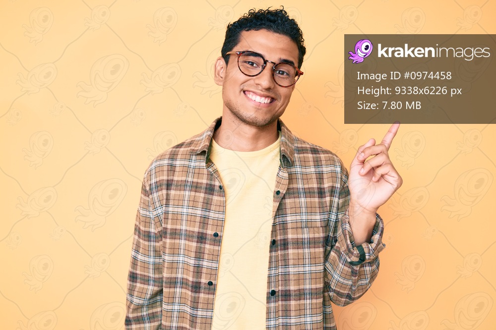Young handsome hispanic man wearing casual clothes and glasses smiling happy pointing with hand and finger to the side 