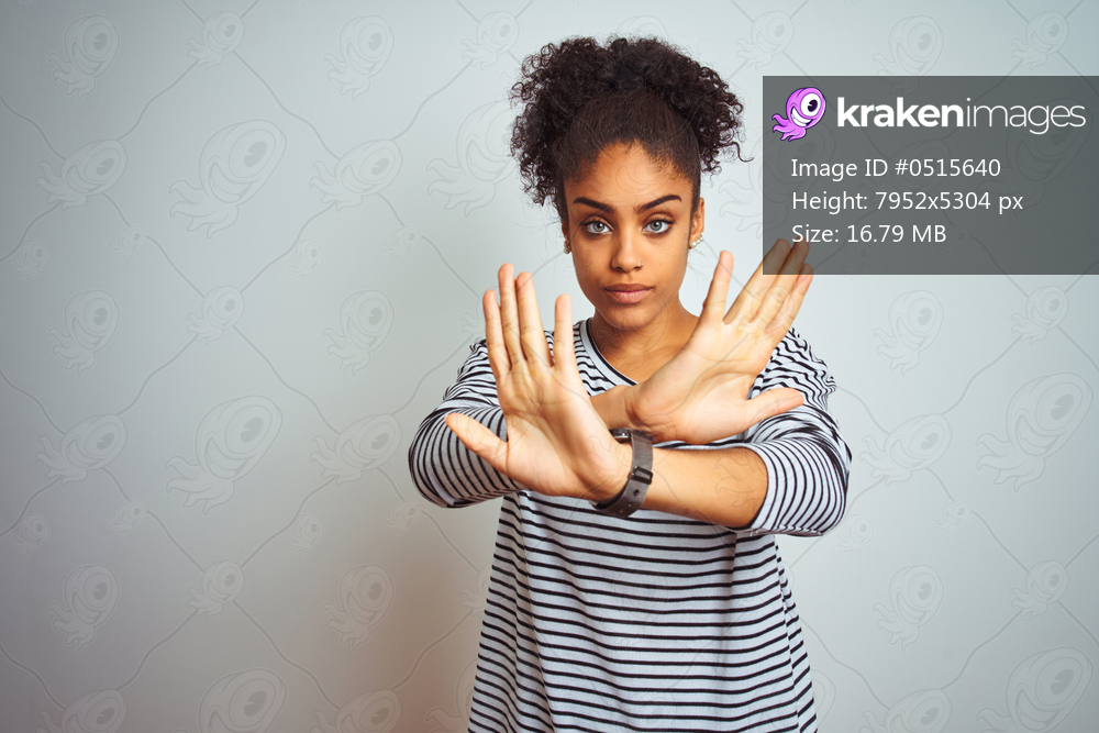 African american woman wearing navy striped t-shirt standing over isolated white background Rejection expression crossing arms and palms doing negative sign, angry face