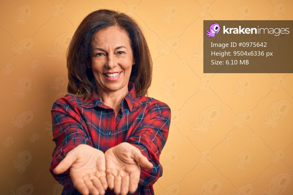 Middle age beautiful woman wearing casual shirt standing over isolated yellow background Smiling with hands palms together receiving or giving gesture. Hold and protection